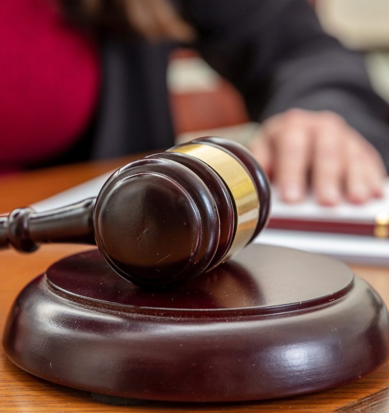 Law courtroom, Judge Bench. Woman sitting, auction gavel and notepad on wooden table, close up.