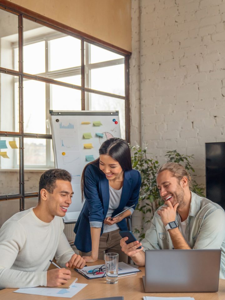 Vertical shot of multiracial business people with laptop and smartphone having meeting in office.